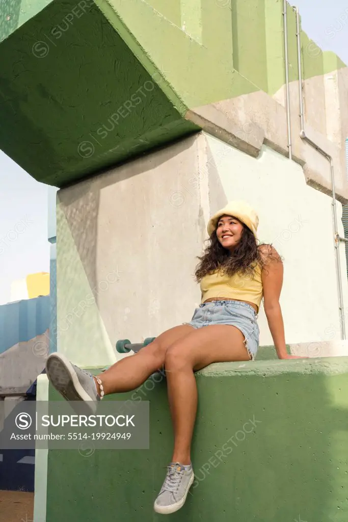 Asian woman sitting on the wall with her skateboard