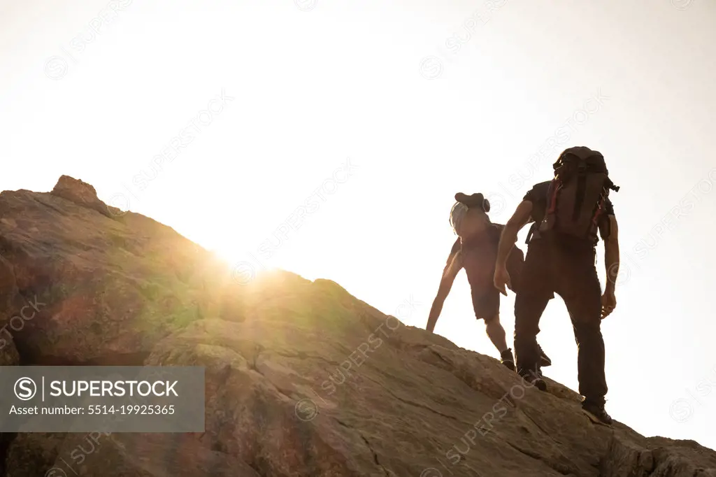 two climbers seen from behind climbing a rock at sunrise