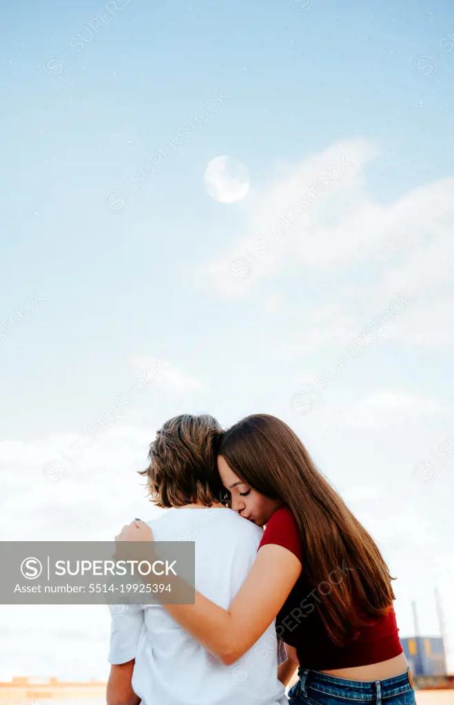 girlfriend kissing her boyfriend's shoulder as she embraces him