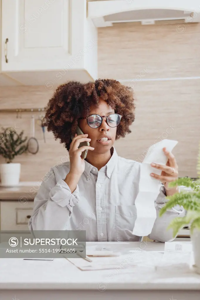 A woman discusses new prices on bills on the phone in the kitchen.