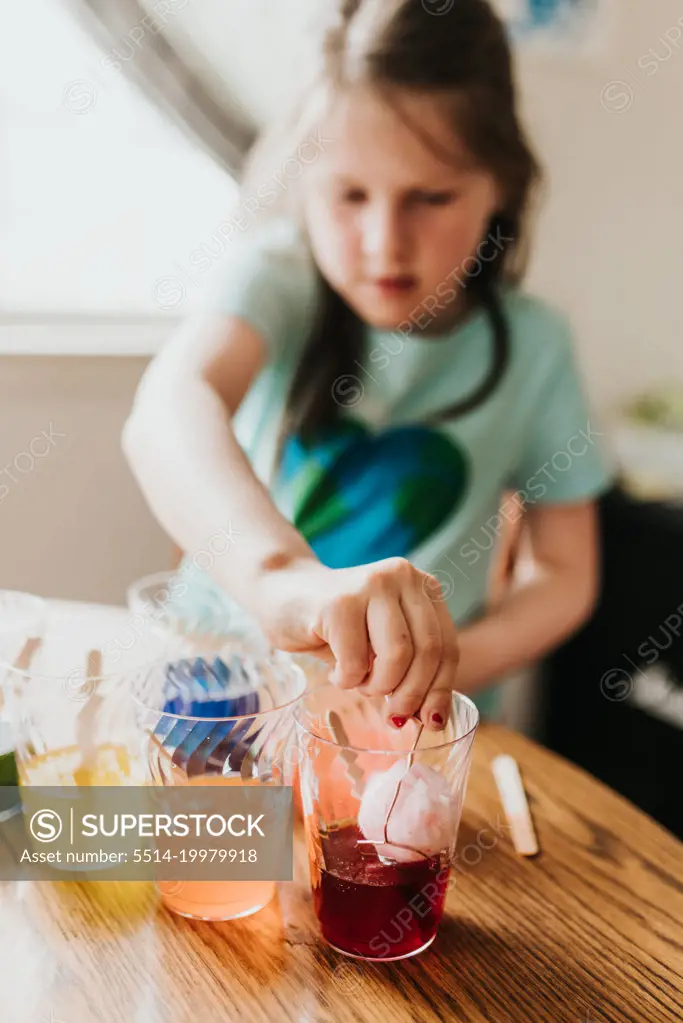 Close up of young girl dying an easter egg red at kitchen table