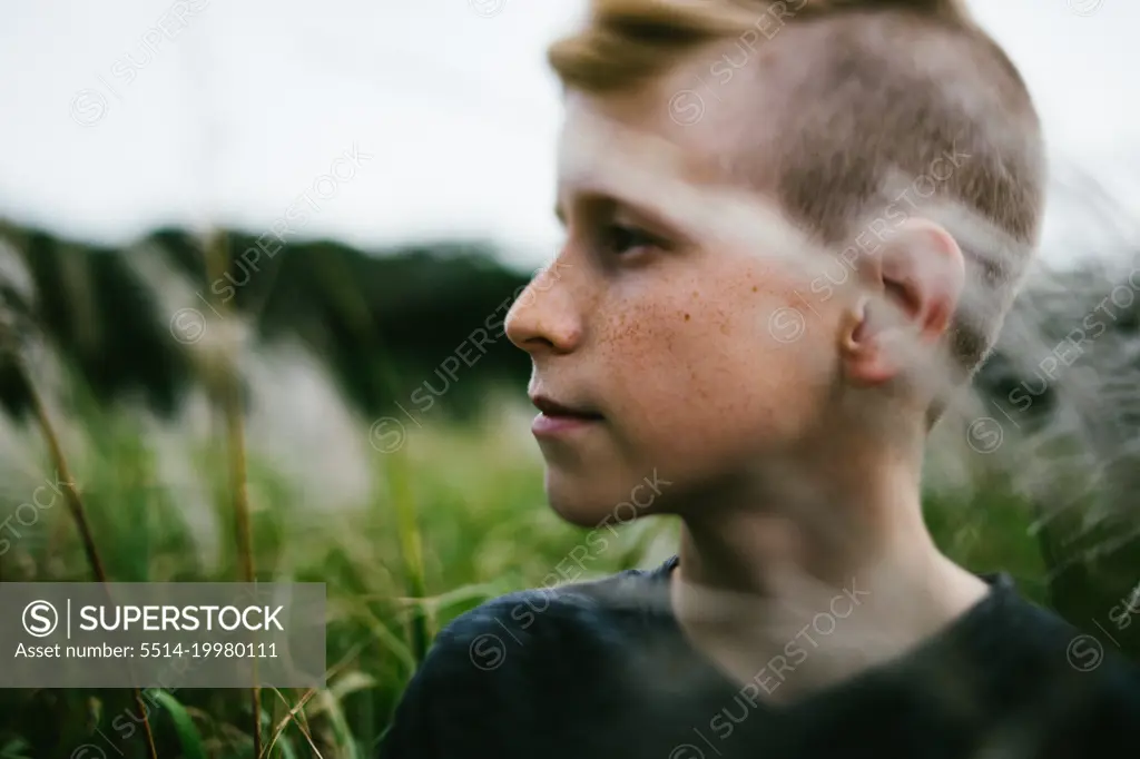 Pre teenage boy outside in nature in grass field