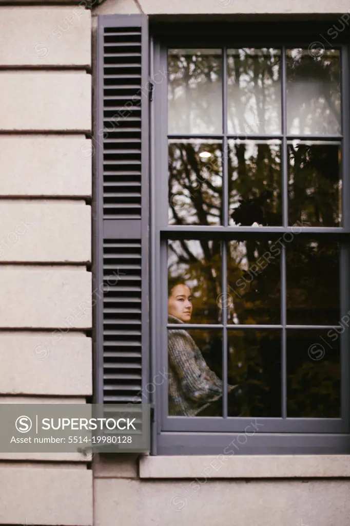Young asian woman looks out window of home in fall season
