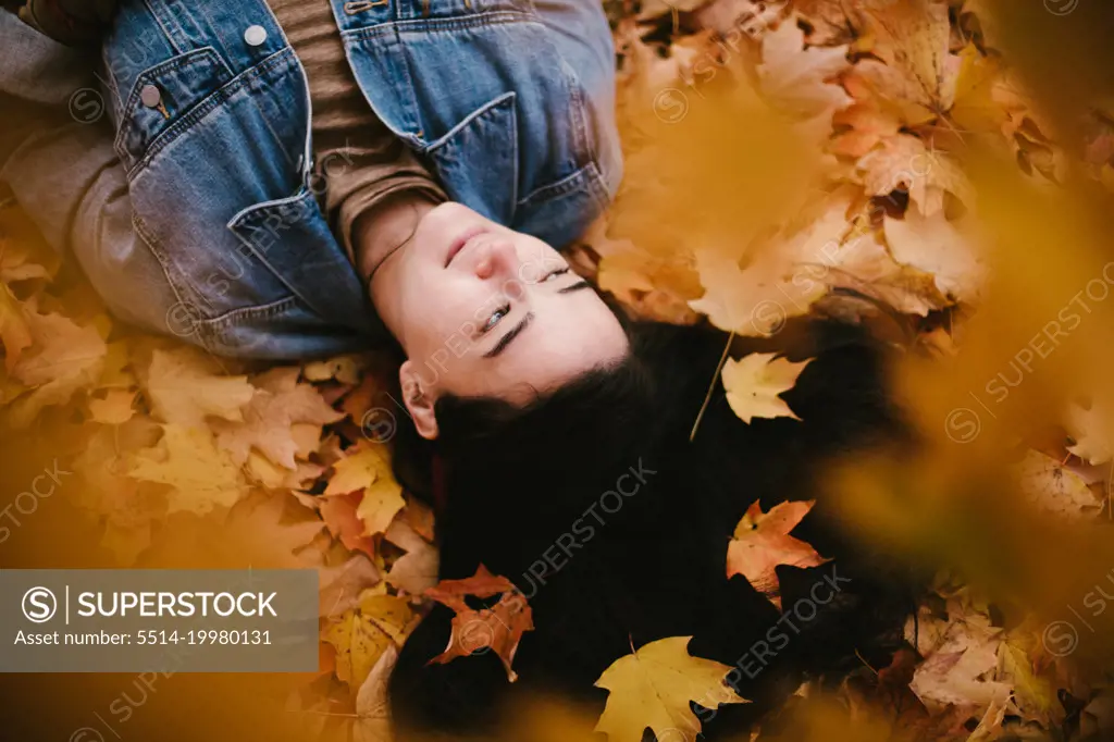 Asian woman lies in pile of fall orange and yellow leaves
