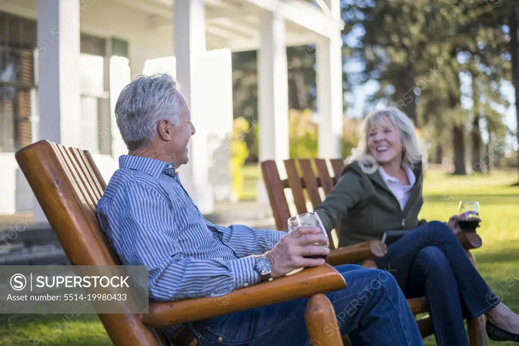 An elderly couple enjoys a glass of wine on the front lawn.