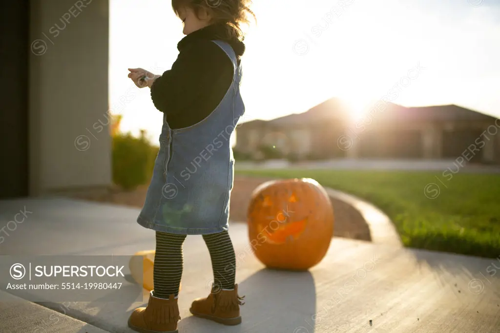 Little girl outside in the sunlight standing by a jack o'lantern