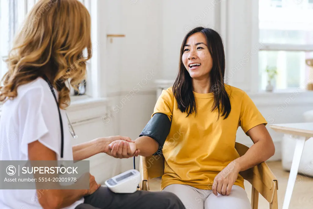 Happy female patient looking at doctor checking her pulse in hospital