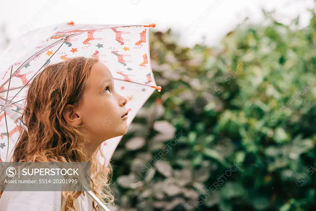 child holding an umbrella looking up at the sky at the rain