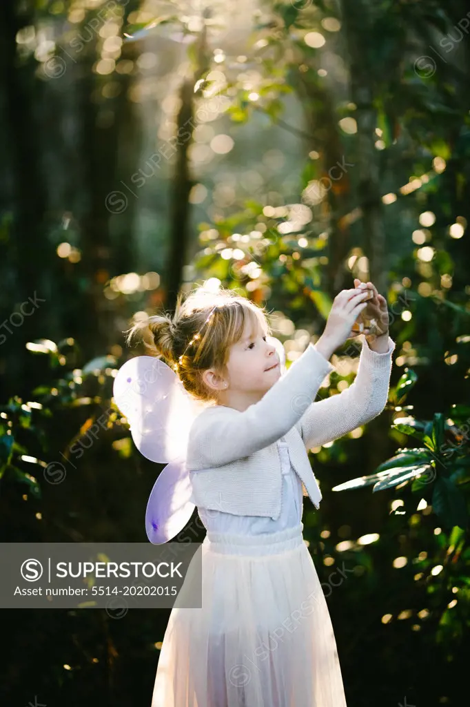 Girl in white angel dress with wings in shining light in forest