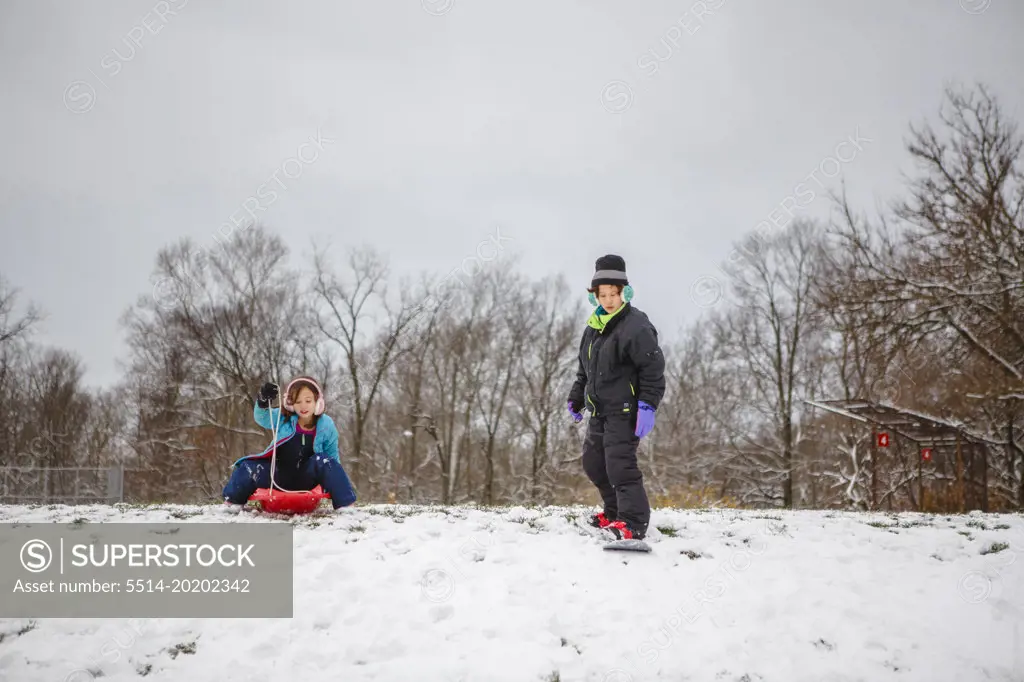 Two children play on snowy hill with sled and snowboard