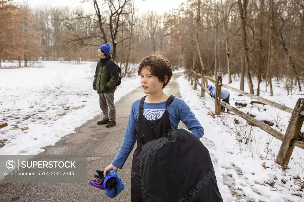 A boy in winter clothes walks on path through woods with family