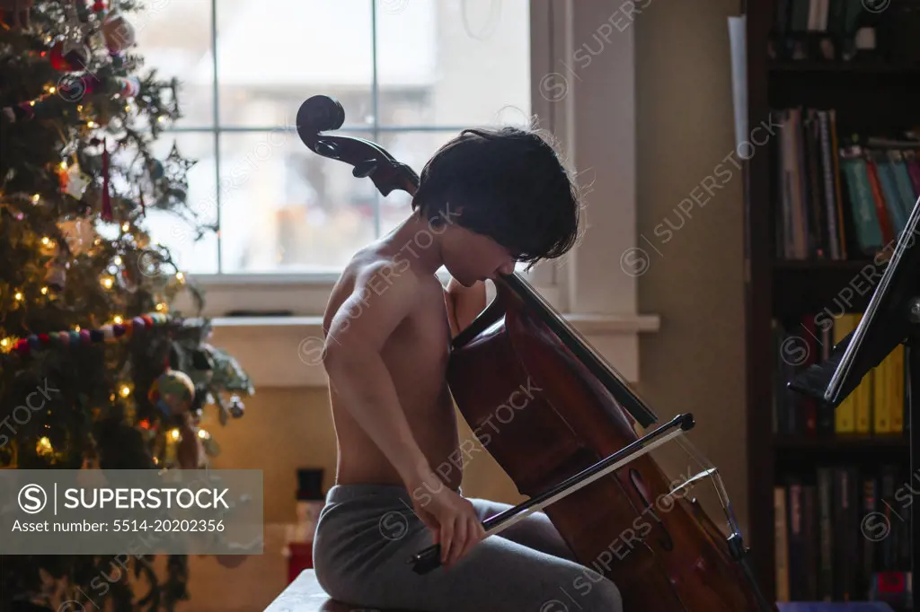 An expressive child plays cello by Christmas tree at home