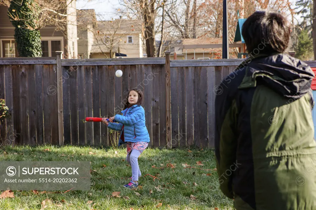 A little girl plays softball with father in backyard in winter