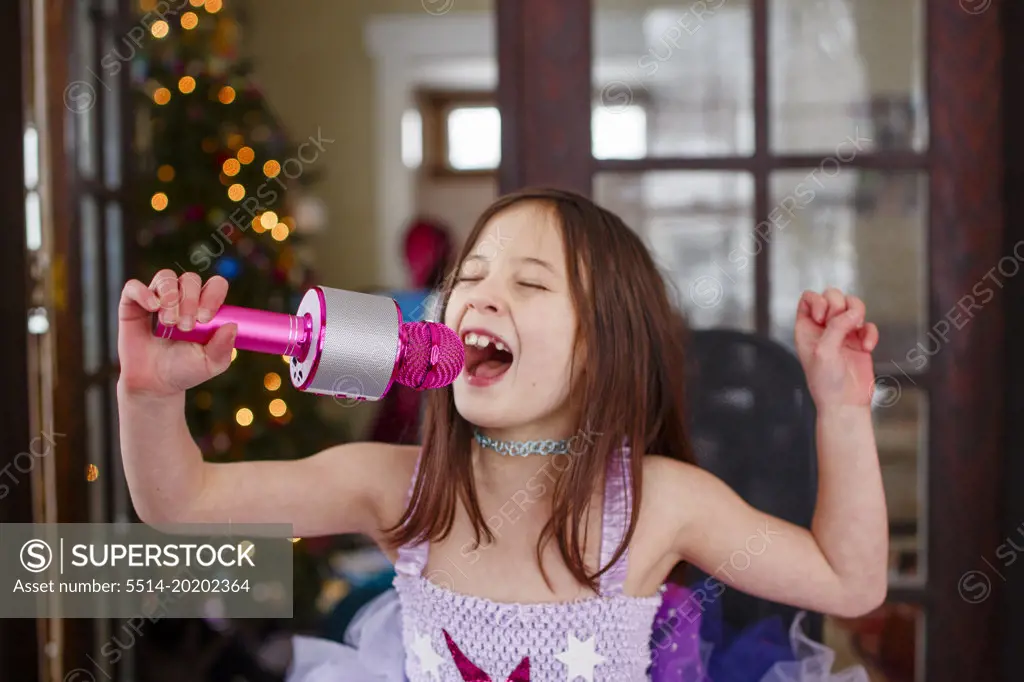A girl in costume sings into a microphone by Christmas tree