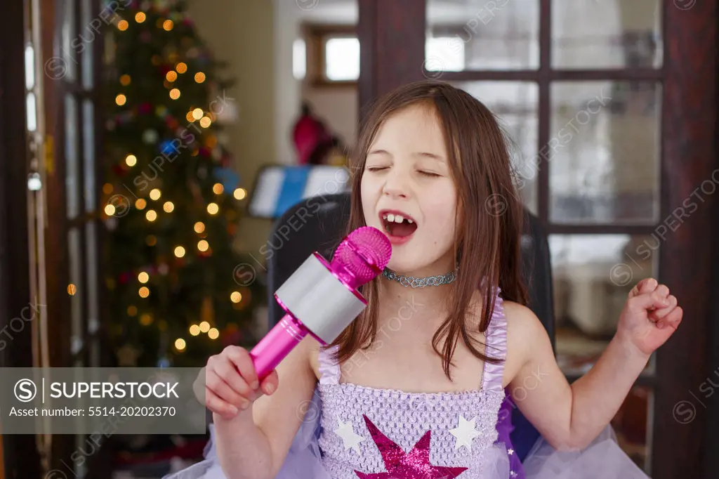 a little girl in costume sings loudly into a microphone at home