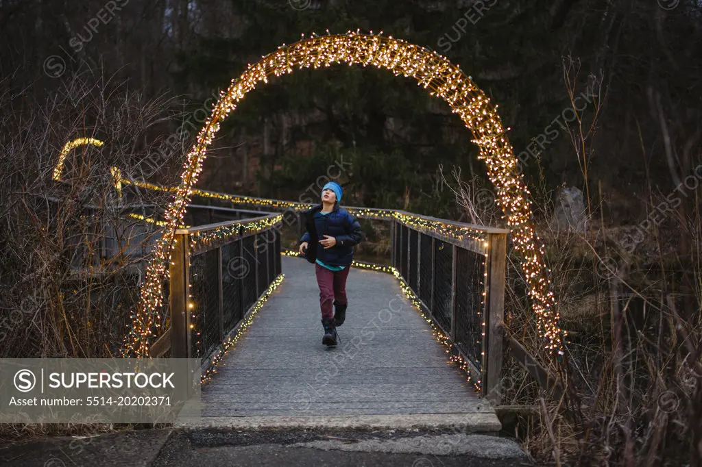 A boy runs through a lit up bridge at dusk in winter