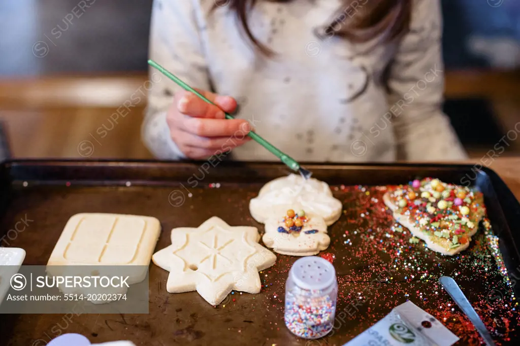 A child decorates a messy tray of Christmas cookies