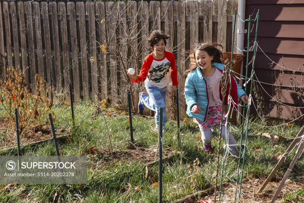 Two children play chase through garden in spring