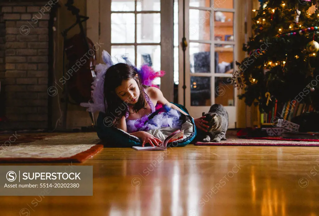 Little girl in costume in sleeping bag by Christmas tree with cat