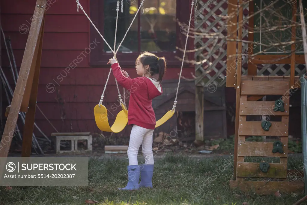 A small child stands in golden light playing on swings