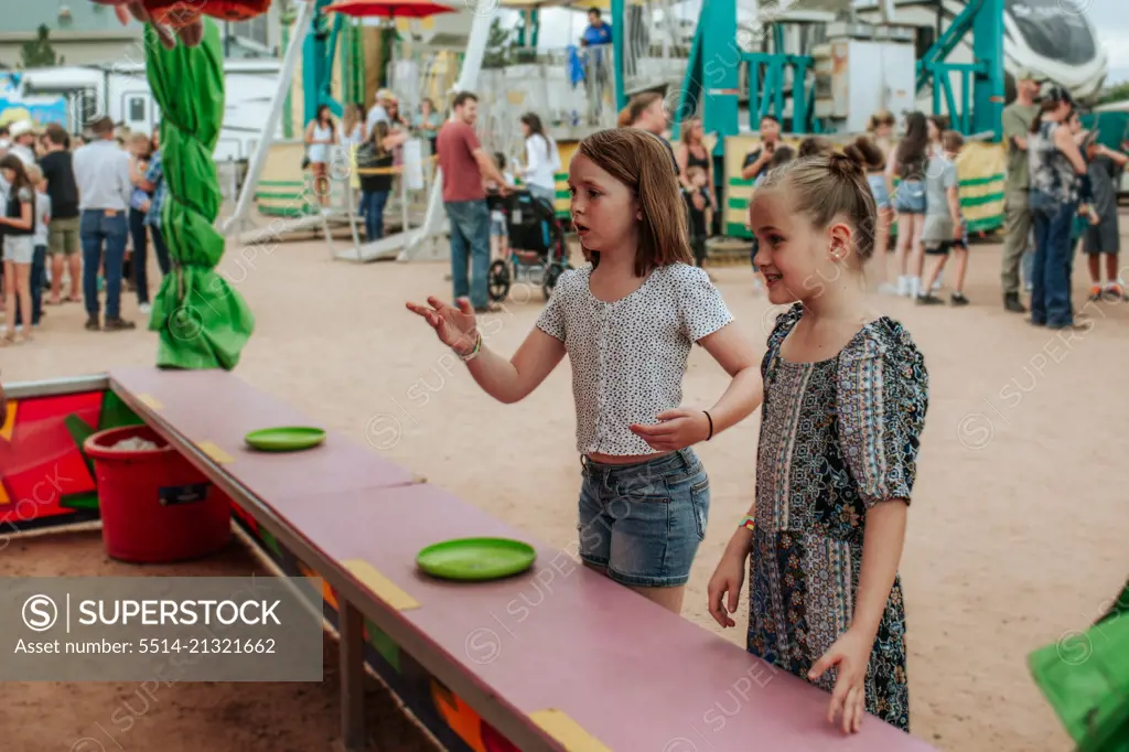 Two young girls playing carnival games at county fair