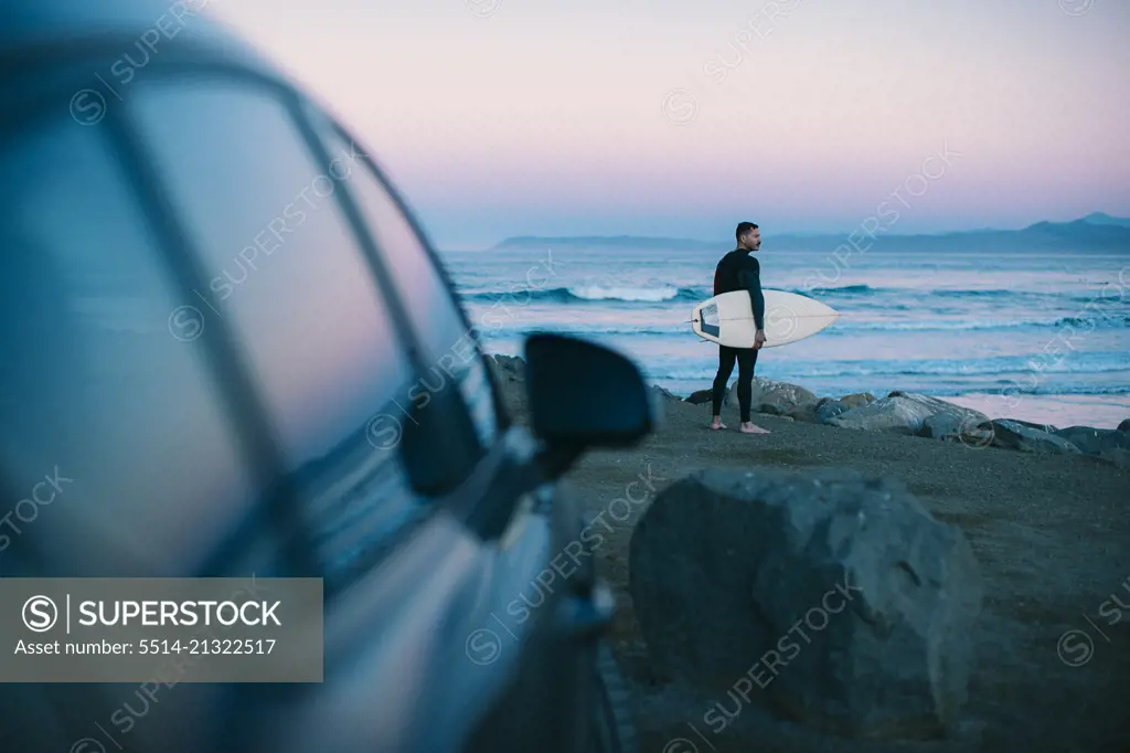 A middle aged surfer looks out towards the beach at blue hour.