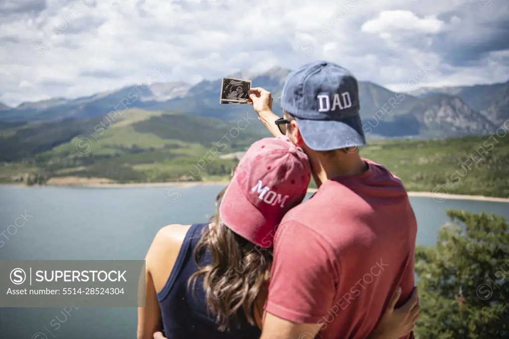Rear view of couple wearing mom and dad caps holding ultrasound