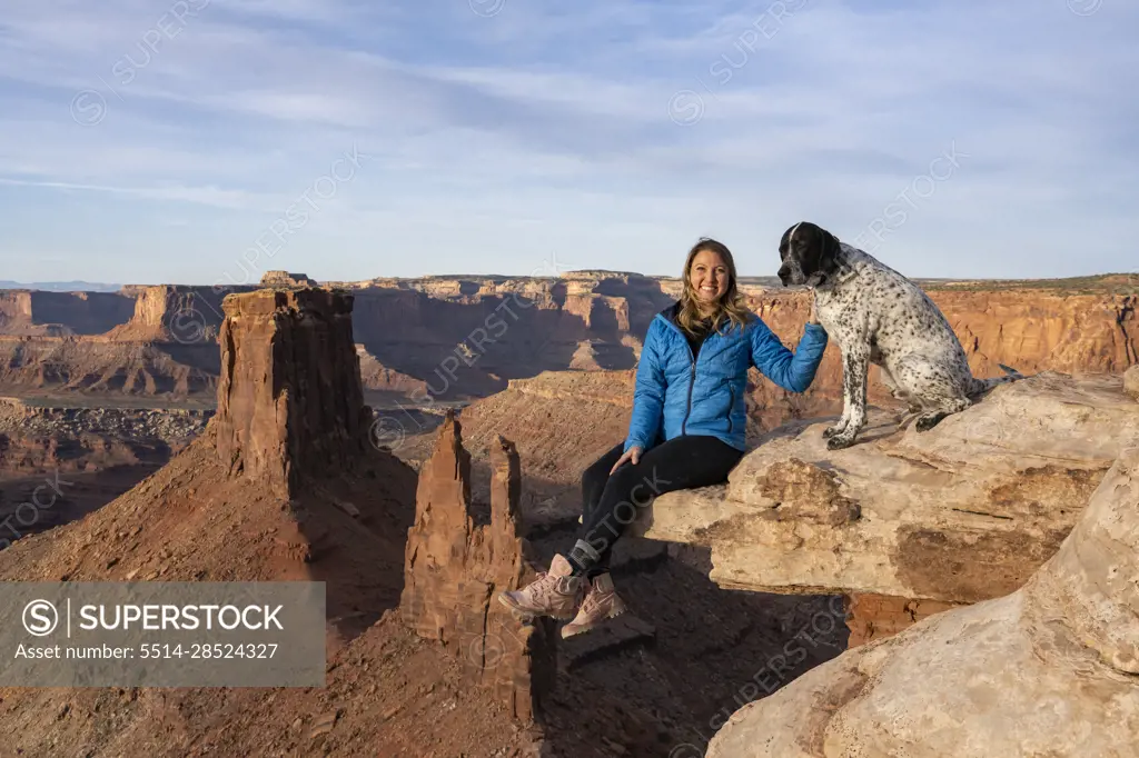 Portrait of cheerful woman sitting with dog on rock in desert