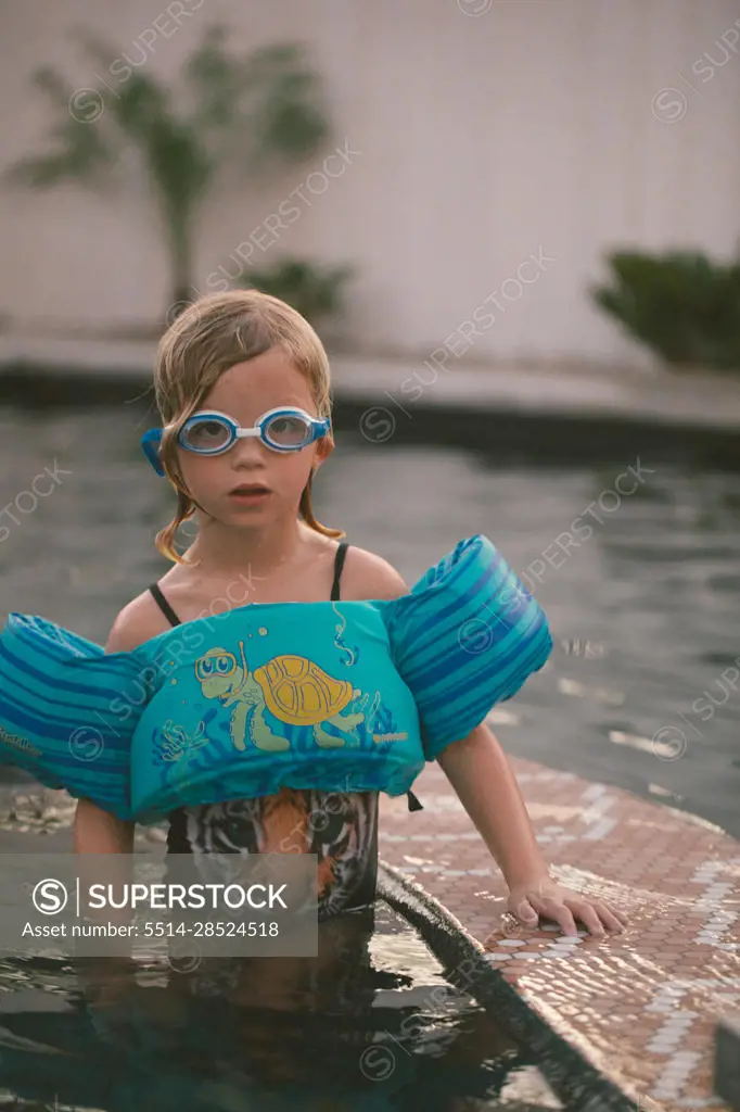 Child in floaty and goggles swimming in a pool in the evening