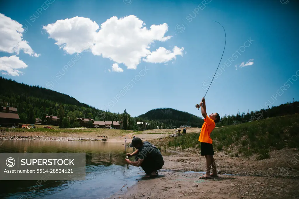 Boy catches fish from lake in mountain on vacation with dad