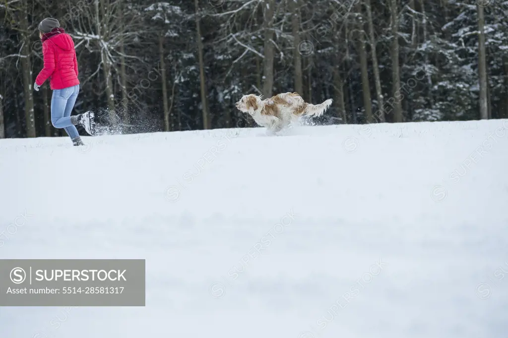 Young woman running with her dog in snowy landscape, Bavaria, Germany