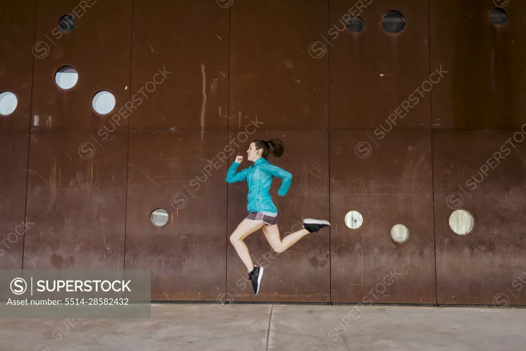Side view of young runner woman sprint and jumping against wall 