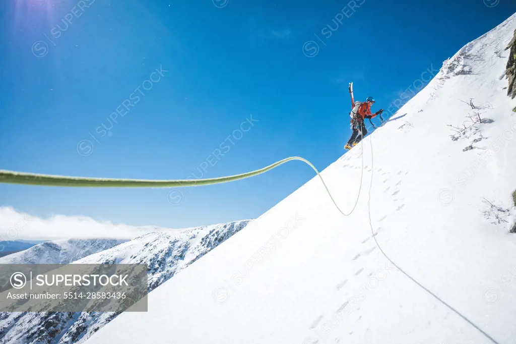 Man walking uphill with ice climbing tools and skis on his back