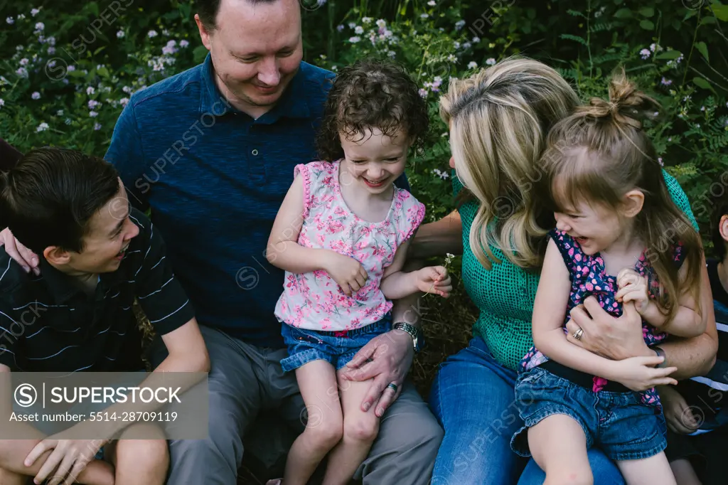 Parents hug and laugh with small children outside in summer