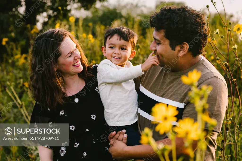 Latino dad and mom laugh with toddler son in flower field