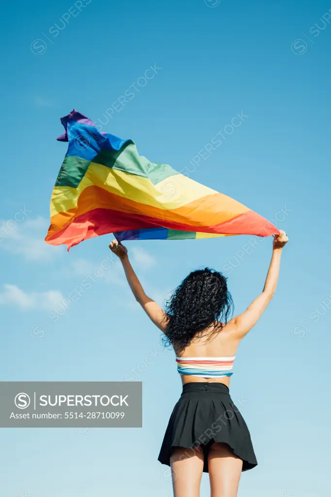 Young woman holding a lgbt flag from behind. Dressed in a colorful top