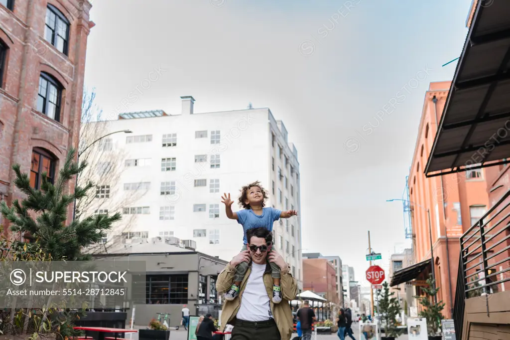 Dad carrying happy biracial toddler on shoulders downtown