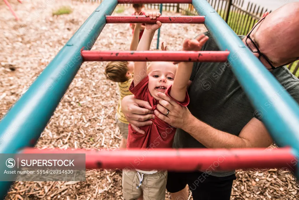 Toddler boy doing monkey bars with help from dad