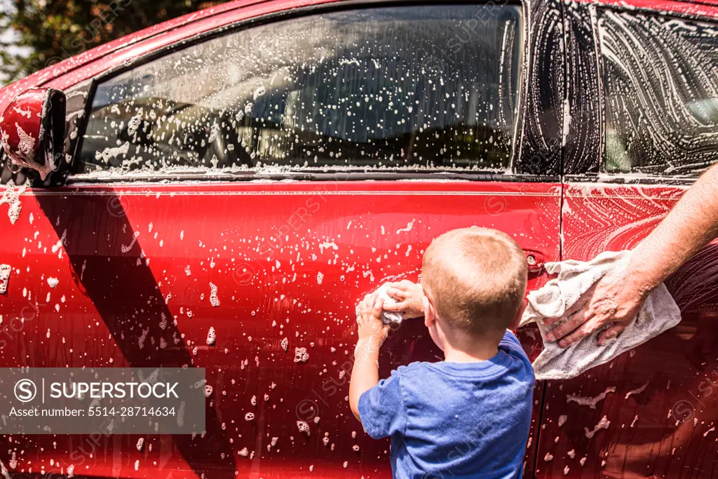 Toddler boy washing red car with help of dad