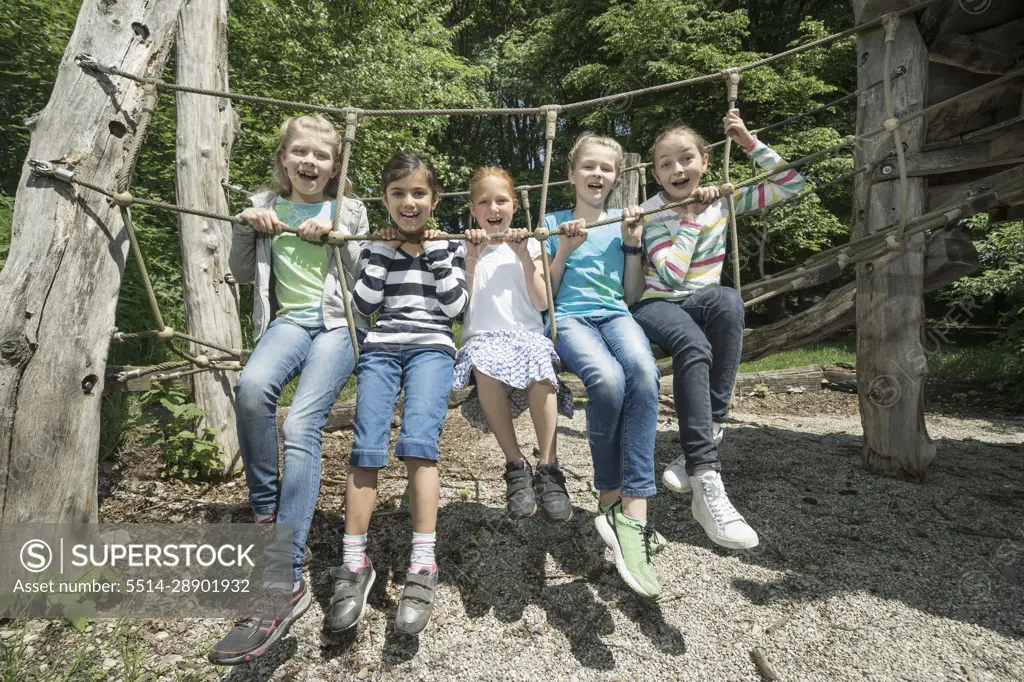 Girls sitting on rope bridge in playground, Munich, Bavaria