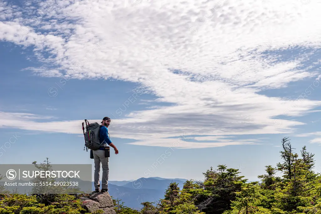 Man in backpack standing on rock at top of mountain.