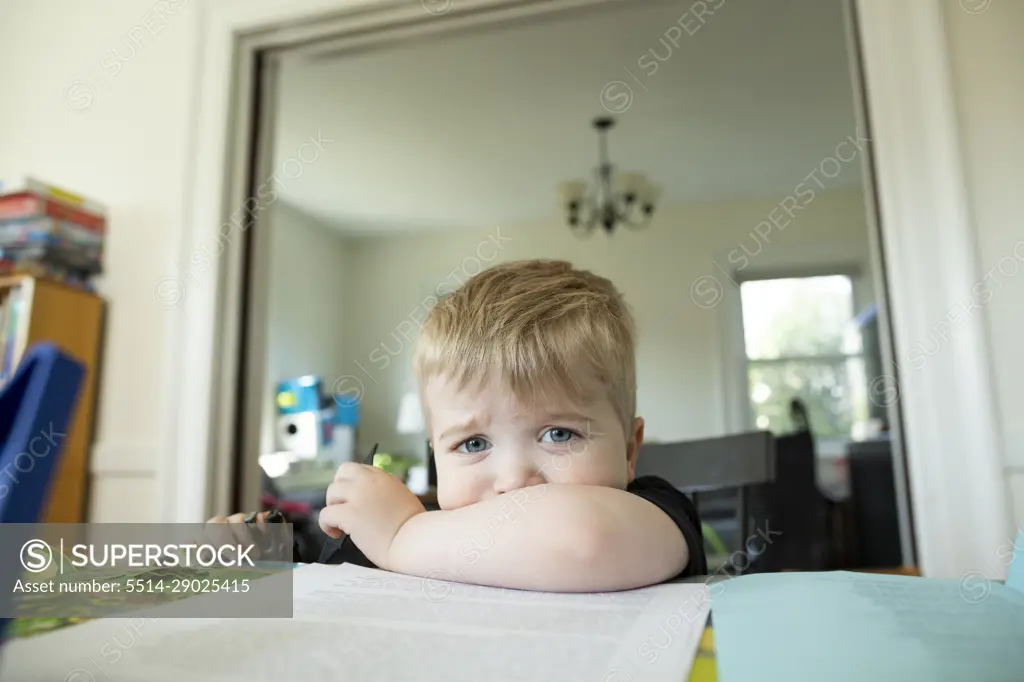 Blonde preschool age boy sitting and pouting with chin resting on arm
