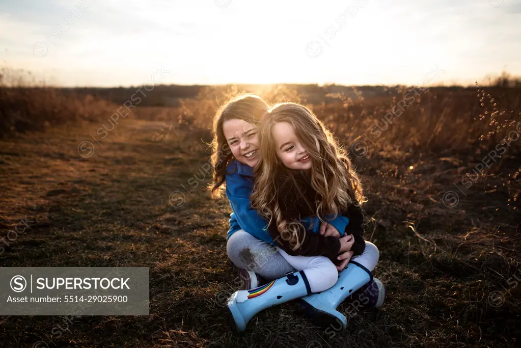 Sisters sitting and smiling in field at sunset