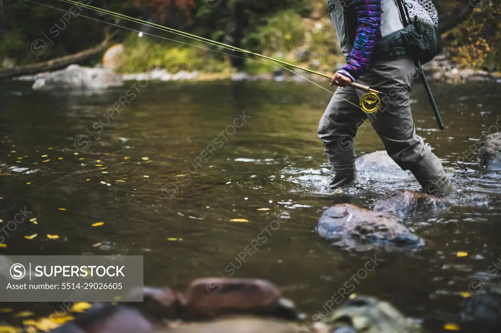 Midsection of woman fly fishing at Roaring Fork River during autumn -  SuperStock