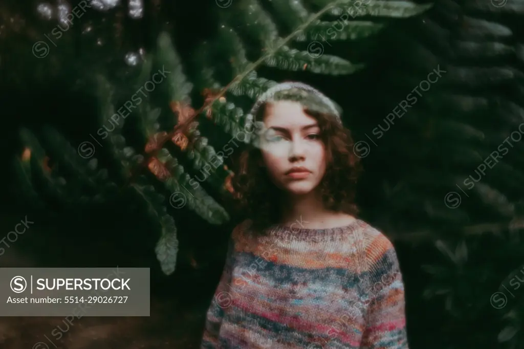 Girl standing behind leaves in sweater and hat