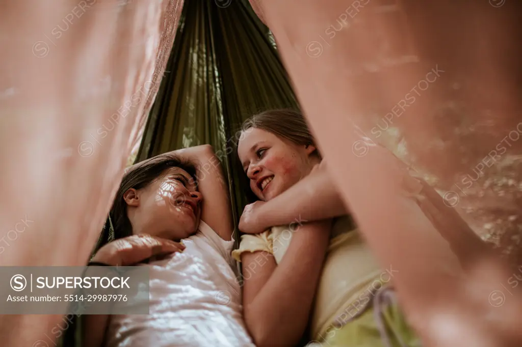 Two teen girls laying in hammock smiling and laughing