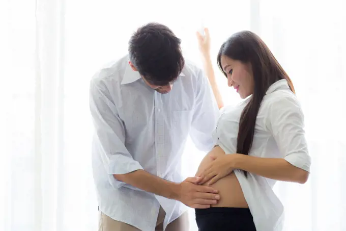 Pregnant mother and father standing hugging holding belly, famil