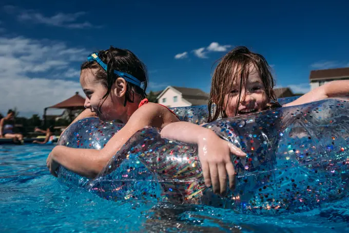 happy girls playing in pool float together while swimming