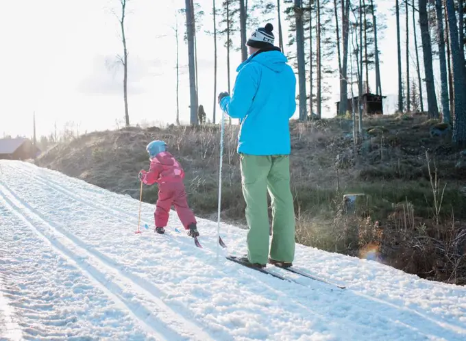 young girl cross country skiing with her dad in Sweden at sunset
