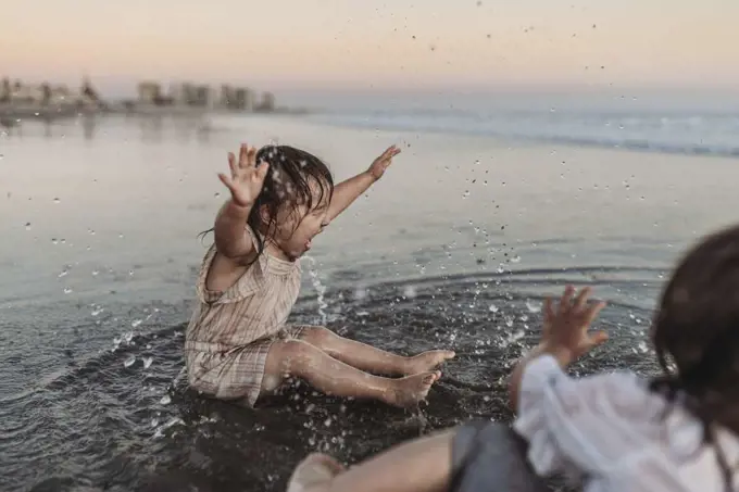 Happy 2 year old girl splashing in ocean water at beach
